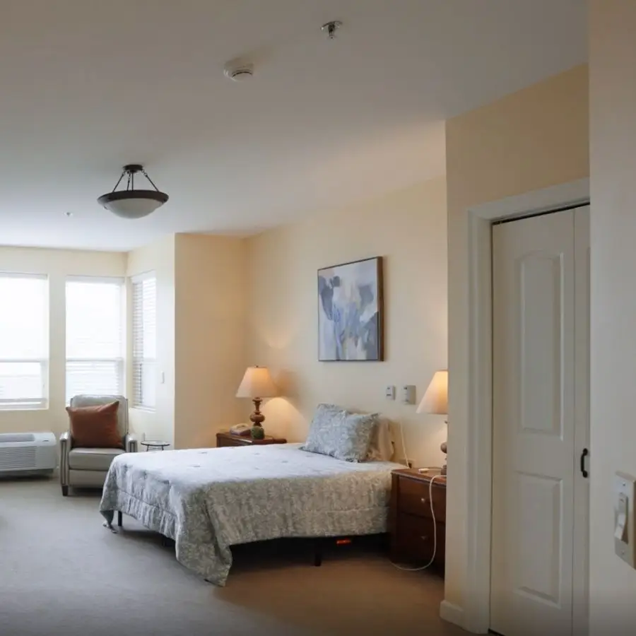 Spacious and well-lit bedroom featuring a queen-sized bed, bedside tables with lamps, and a cozy armchair, complemented by soft neutral walls and large windows.