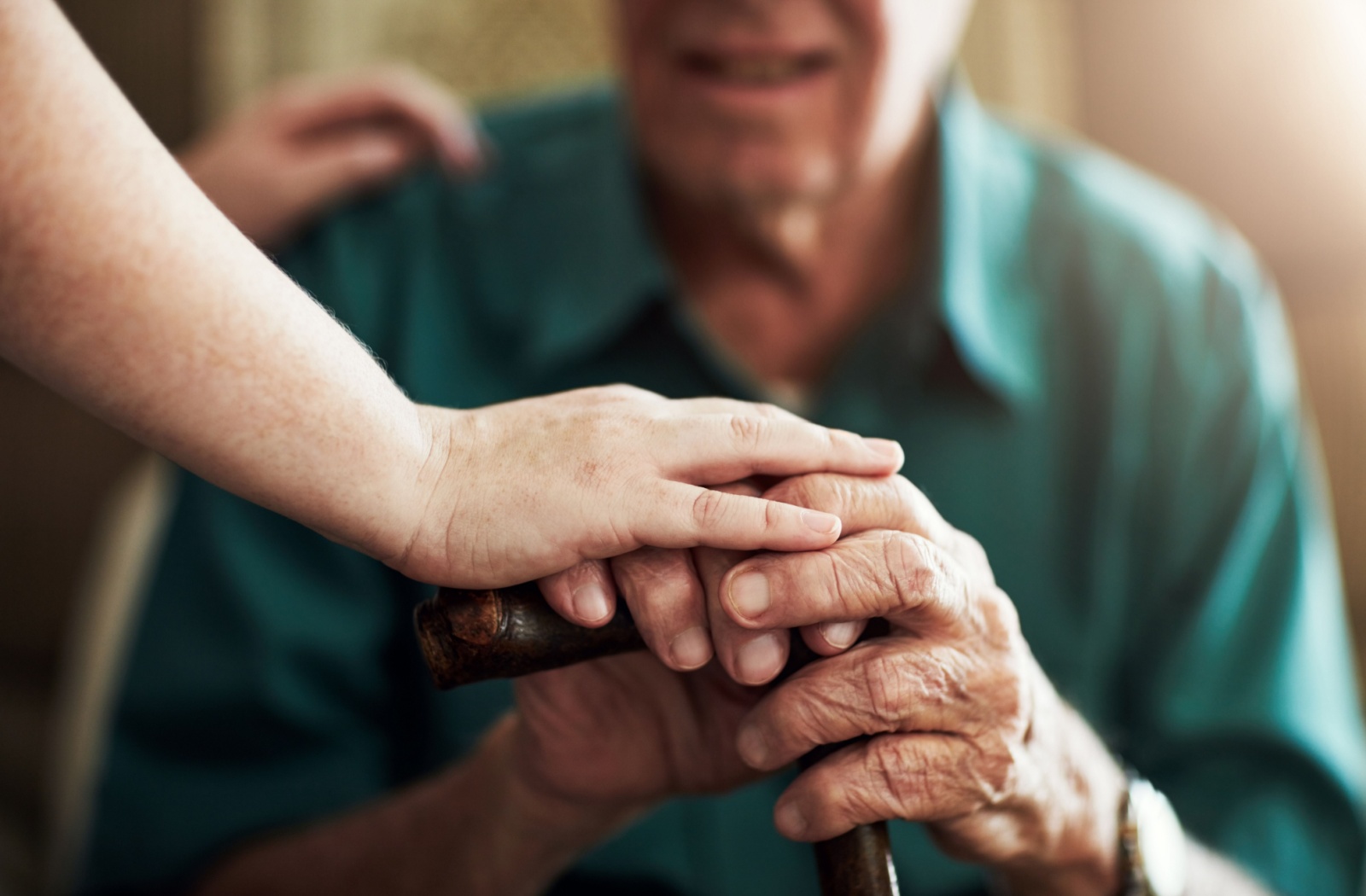 Close-up of a caregiver's hand resting on an older adult's hand holding a cane.