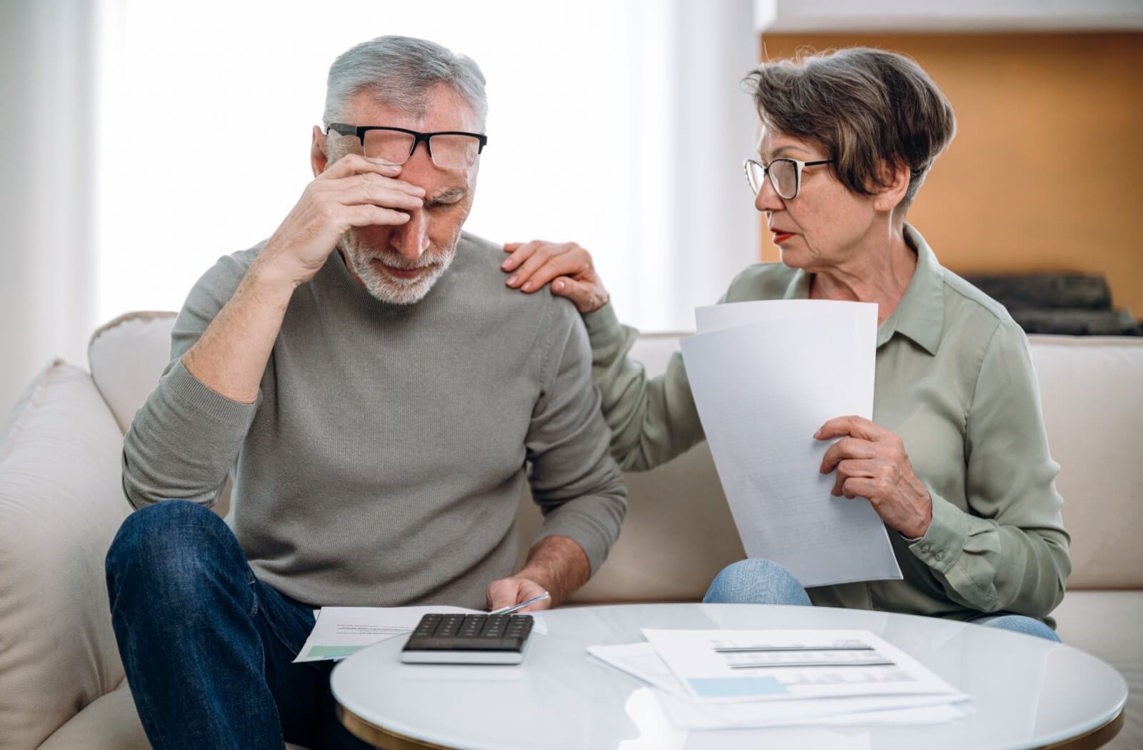 Concerned older couple reviewing documents and using a calculator at home.