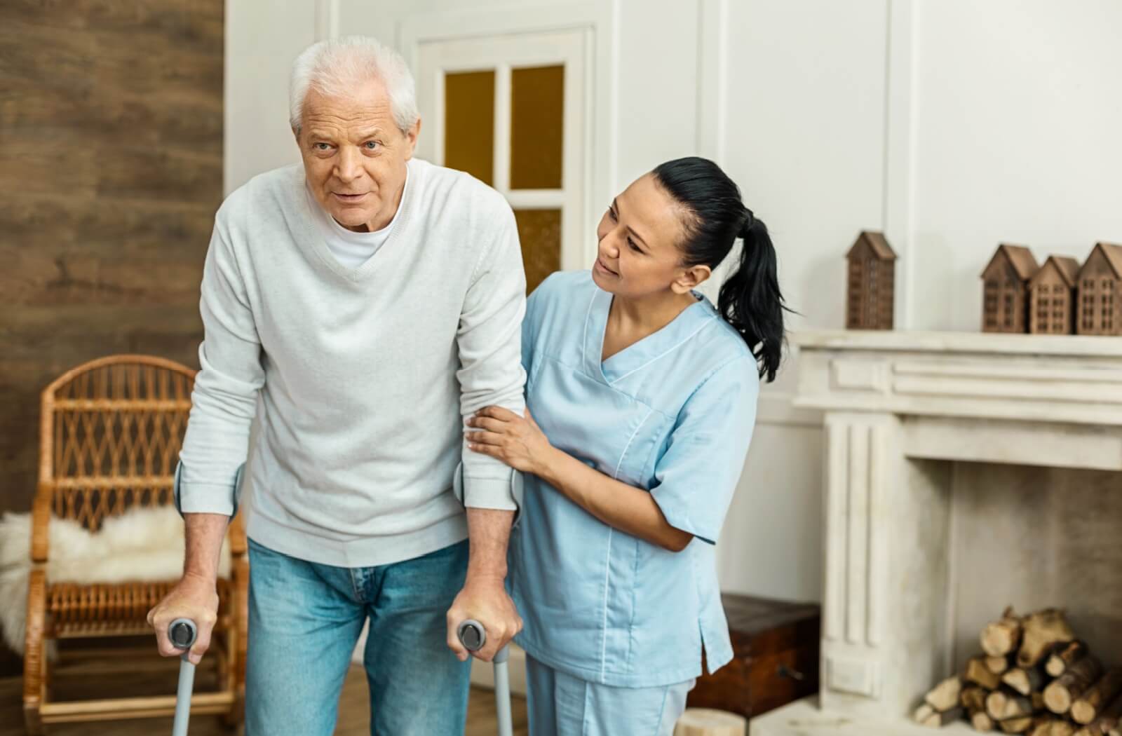 Caregiver assisting an older adult using crutches in a living room.