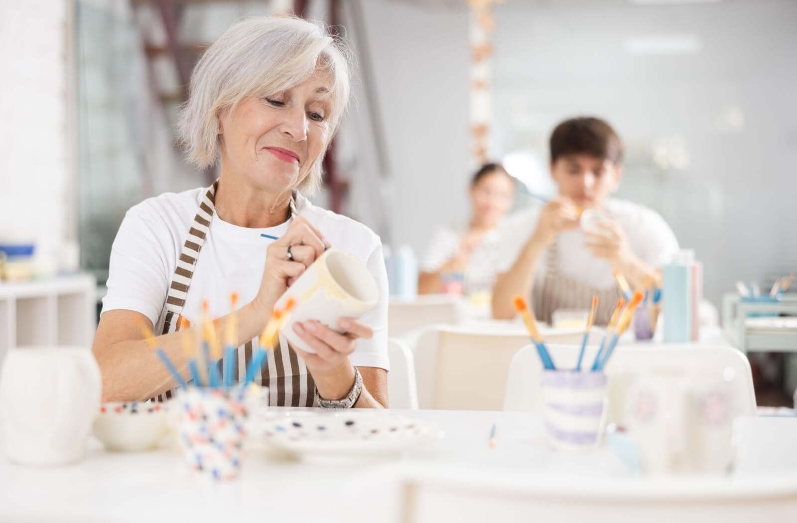 A senior woman paints a piece of pottery at a craft studio in a senior living community