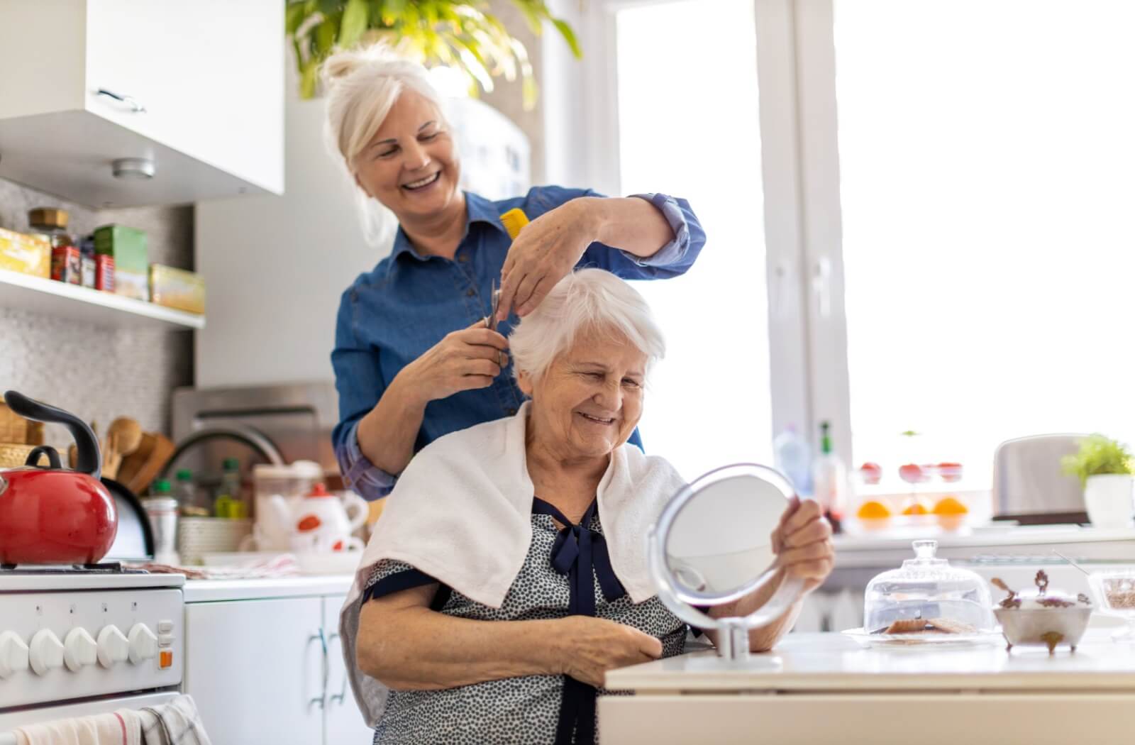 A smiling adult cuts their senior parent’s hair in the kitchen as a means of helping with hygiene after a dementia diagnosis