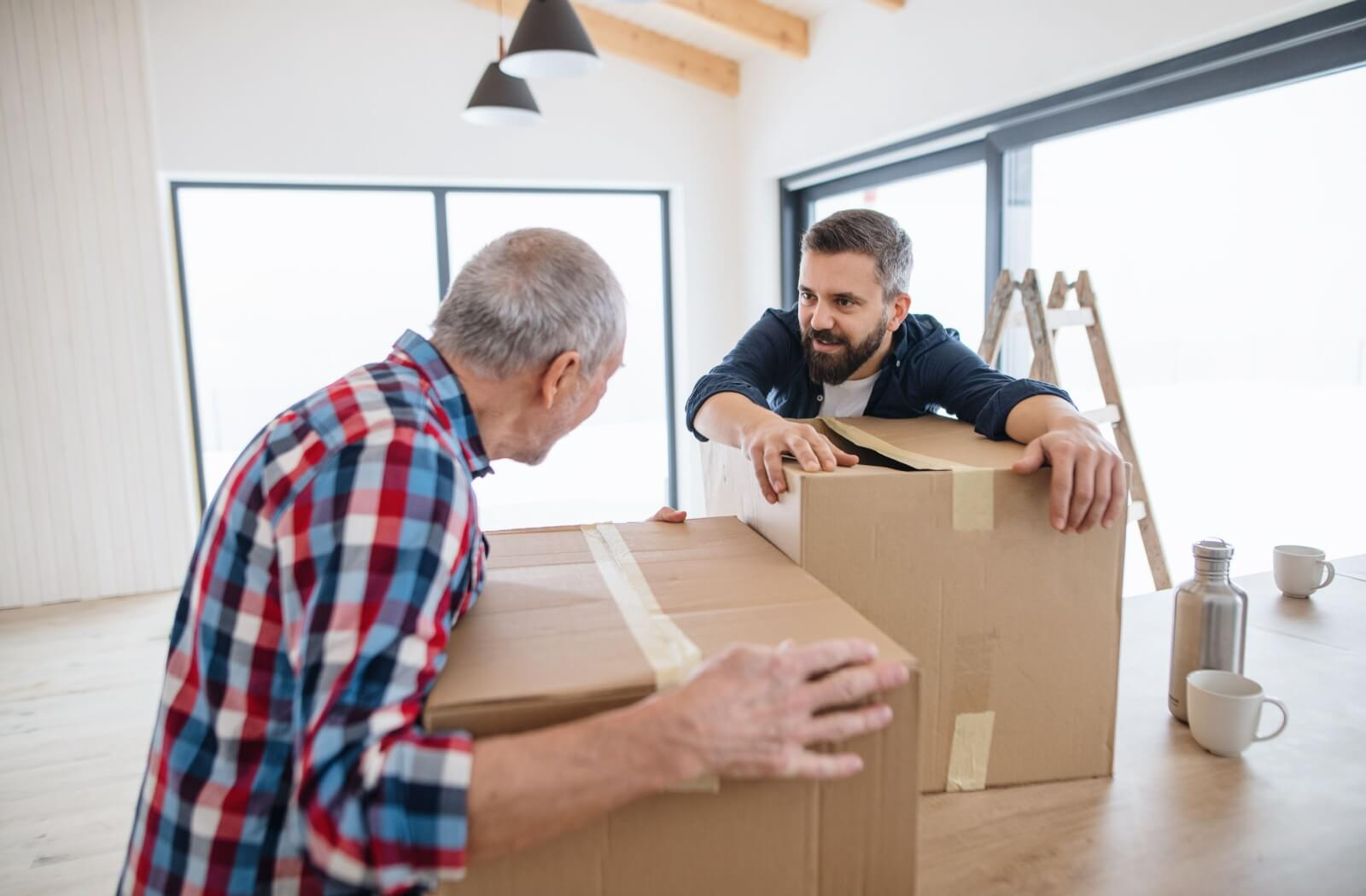 An adult helps their older parent downsize their home by physically helping move heavy boxes